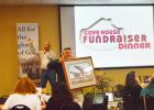 CCLP/LYNETTE SOWELL - Brian Hawkins, executive director of Cove House holds up a framed print during the live auction as he helps raise money for the homeless shelter and free clinic Monday evening