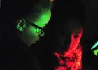 Joelle Spinks and Victoria Ventura, fourth graders at Martin Walker Elementary School, use a black light to search for clues on a piece of paper containing a sentence with comma splices. 